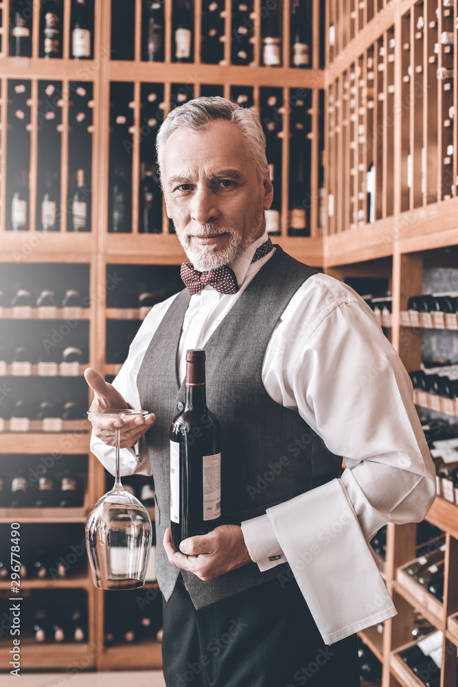 Wall mural Sommelier Concept. Senior man walking with bottle and wine glass upside down smiling joyful