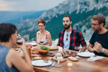 Friends and family gathered for picnic dinner for Thanksgiving. Festive young people celebrating life with red wine, grapes, cheese platter, and a selection of cold meats