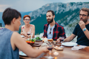 Friends and family gathered for picnic dinner for Thanksgiving. Festive young people celebrating life with red wine, grapes, cheese platter, and a selection of cold meats