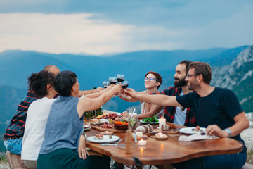 Friends and family gathered for picnic dinner for Thanksgiving. Festive young people celebrating life with red wine, grapes, cheese platter, and a selection of cold meats