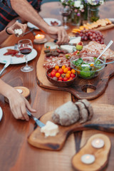 Friends and family gathered for picnic dinner for Thanksgiving. Festive young people celebrating life with red wine, grapes, cheese platter, and a selection of cold meats