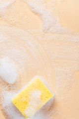 Yellow sponge for cleaning in foam on a soft beige background, top view, free space for text. House cleaning with sponge. Cleaning concept, copy space.