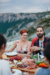 Friends and family gathered for picnic dinner for Thanksgiving. Festive young people celebrating life with red wine, grapes, cheese platter, and a selection of cold meats