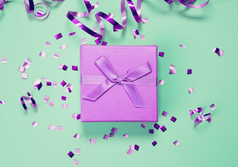 Present box on mint background with shiny confetti. Holiday and festive backdrop. Flat lay style