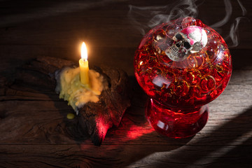 Halloween welcome drink with skull and hot transparent ball and candlelight on old wooden table