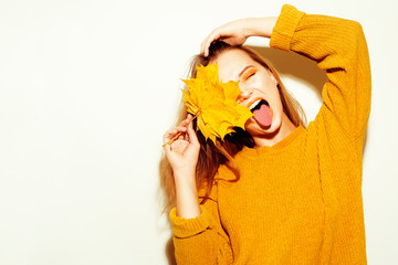 A girl in a yellow autumn sweater and leaves the trees goes crazy, has fun, smiles, covers her face with a leaf. Autumn, autumn discounts, autumn clothes.