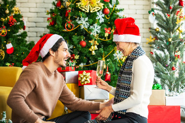 Obraz na płótnie Canvas Happy couple woman and man in santa hat enjoying and celebrating family Christmas party together with drinking white wine or champagne and toasting wine glass with decoration Christmas tree background