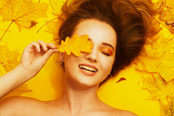 Autumn photo of a happy girl. Girl autumn leaf closes her eyes and smiles. Happy girl, fall discounts, bright autumn photo. Autumn yellow / orange make-up. Gold earrings, golden autumn.