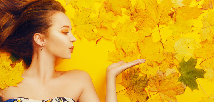 Autumn magical girl. The girl sends a kiss, blows in the direction. Happy girl, fall discounts, bright autumn photo. Autumn yellow / orange make-up. Gold earrings. The girl lies in the leaves
