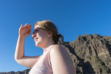 Pretty teenager searching and staring, protect with the hand his face from the sun. Blond Lady with glasses smiley, touching her forehead to contemplating far. Looking far in the mountain
