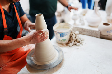 Hands of young potter, was produced on range Hands of a potter skillfully making a pot of white clay.