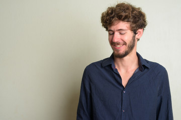 Happy young bearded businessman with curly hair thinking and looking down