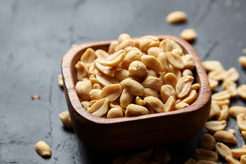 Wooden bowl with roasted peeled peanuts, salty beer snack on dark background