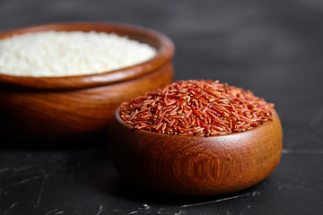 Red and white rice in a wooden bowls on black stone table. Dry uncooked grains. Ingredient for cooking various dishes