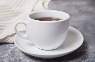 Close up of cup of coffee and knittead white plaid on the gray background