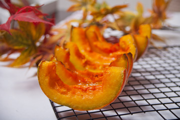 Fresh pumpkin cut in pieces of a oven metal baking rack with herbs and spices with colorful autumn leaves on the background
