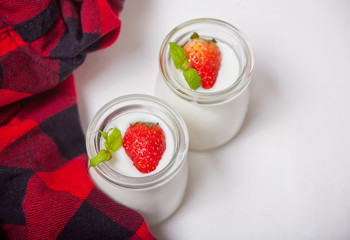 Two portions natural homemade yogurt in a glass jar with fresh strawberry with red checkered napkin on the white background
