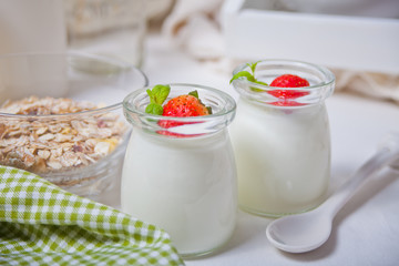 Two portions natural homemade yogurt in a glass jar with fresh strawberry and muesli nearby