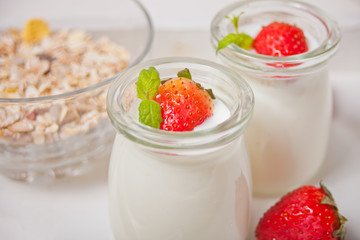 Two portions natural homemade yogurt in a glass jar with fresh strawberry and muesli nearby