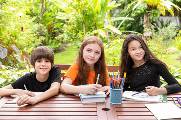 Children, boy and girl, doing homework and drawing together in garden at home, looking at camera