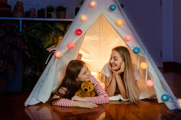 Happy mother and daughter inside tepee tent in bedroom, enjoy talking and story telling; family...
