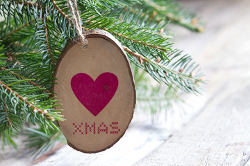 Wooden adornment with heart and xmas inscription hanging on christmas tree