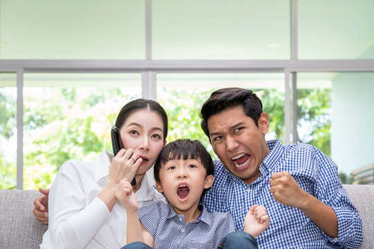 Happy Asian family watching TV together in living room at home; frighten by horror movie