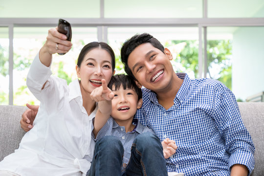 Happy Asian family watching TV together in living room at home; cheerful and fun with movie