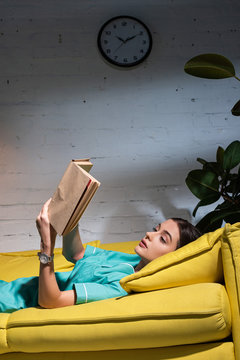 Attractive Nurse In Uniform Lying On Sofa And Reading Book During Night Shift