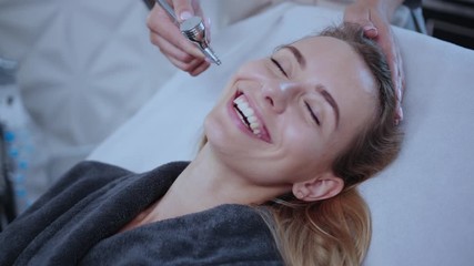 Happy smiling young woman in beauty salon enjoying skincare mesotherapy medical facial massage on spa procedure. Professional hardware cosmetology.