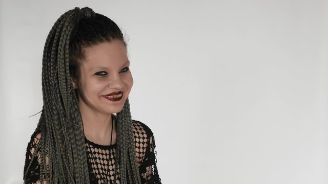 A weird gothic girl with long grey afro braids and a dark make up is smiling and then  laughing. A creative concept for cosmetics, afro hairstyle haidresser's or a fashion company.