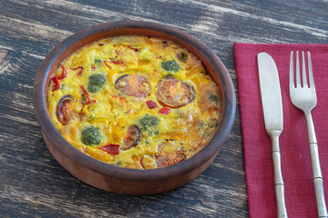 Ceramic bowl with vegetable frittata, simple vegetarian food. Frittata with egg, tomato, pepper, onion, broccoli and cheese on wooden table. Italian egg omelette