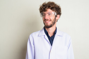 Face of happy young bearded man doctor as scientist with protective glasses thinking