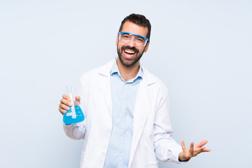 Young scientific holding laboratory flask over isolated background smiling