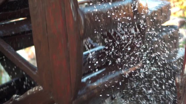 The pressure of water rotates an old water mill. Spray flying in different directions