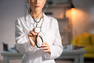 cropped view of doctor in white coat holding stethoscope during night shift