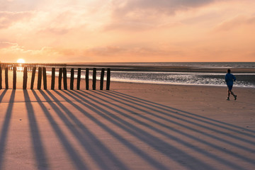 man running in front of a beautiful sunset on the coast in northern France
