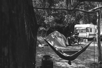 Girl resting in a hammock. Day time camp in the forest, trailer house and touristic tent. adventure motorcycle tour, seasonal vacation. copy space