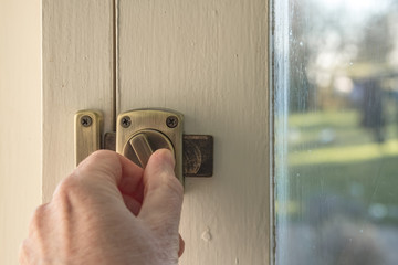 Adult male locking a retrofit, crime prevention lock to a wooden garden door. Detail of the brass...