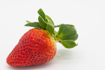 Cluster of organically grown and ripe Strawberries, showing one of the large Strawberries with a bite taken out of it. Shown together with there great leaves as seen on a plate.