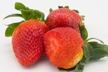 Cluster of organically grown and ripe Strawberries, showing one of the large Strawberries with a bite taken out of it. Shown together with there great leaves as seen on a plate.
