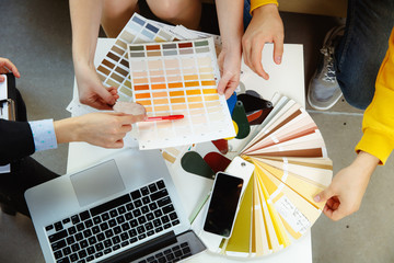 Interior designer working with young couple. Lovely family and professional designer or architector discussing conept of future interior, working with colour palette, room drawings in modern office.