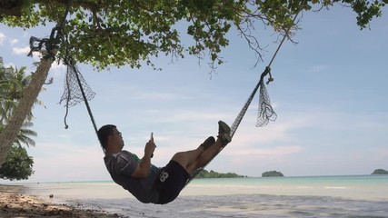 A man lying in hammock while using smart phone near the sea, Lockdown. footage video 4k b roll scene. relaxing and summer time.