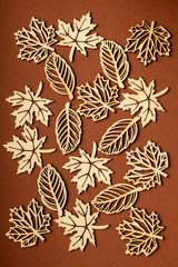 Different types of delicate light brown wooden leaves on textured brown cardboard, top view or flat lay with laser cut wooden objectives