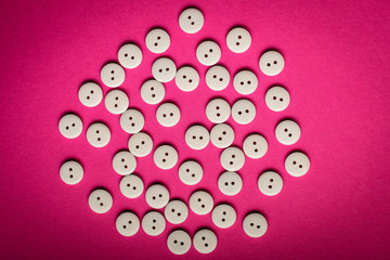 Large group pf delicate light white wooden buttons on pink magenta textured cardboard  background, displayed centred, top view with space for text around, flat lay with laser cut wooden objects