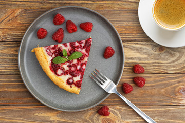 Piece of homemade raspberry pie with yogurt filling and cup of coffee on wooden table. Top view.