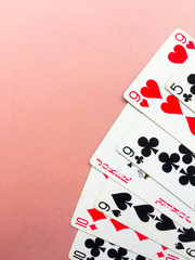 Cards for playing poker lie in the coner of a pink background. Place for text.