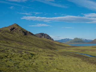 Fototapeta na wymiar Beautiful landscape of blue Alftavatn lake and river with snow covered mountains and green hills and blue sky background. Summer landscape of the Fjallabak Nature Reserve in the Highlands of Iceland