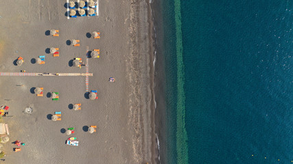 Aerial drone top down photo of famous organised with umbrellas and sunbeds black sand beach and bay of Perissa village, Santorini island, Cyclades, Greece