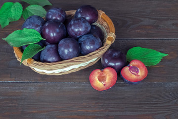 ripe plums in a wicker basket closeup. plums and plum halves on a wooden background. background with fresh plums.